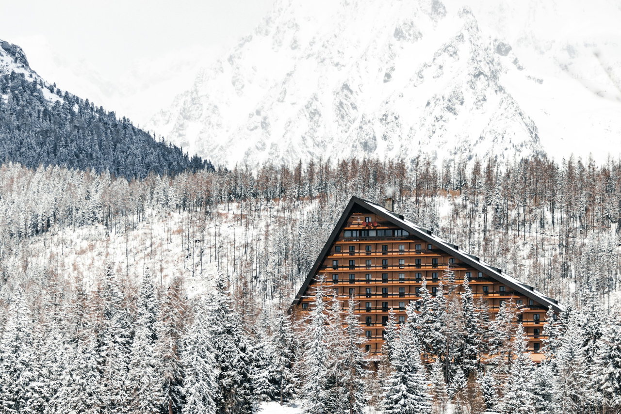 Holzverkleidetes Berghotel mit steilem Dach inmitten verschneiter Wälder, dahinter schneebedeckte Gipfel