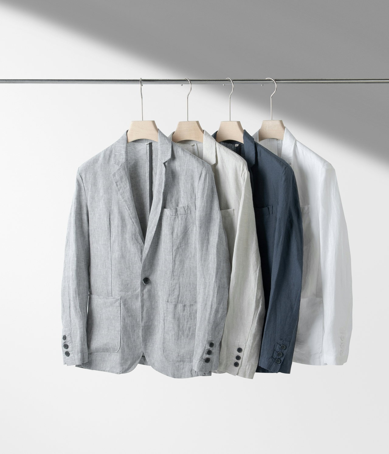Mehrere unstrukturierte Blazer in Grau und Weiß auf Bügeln an einer Stange vor heller Wand