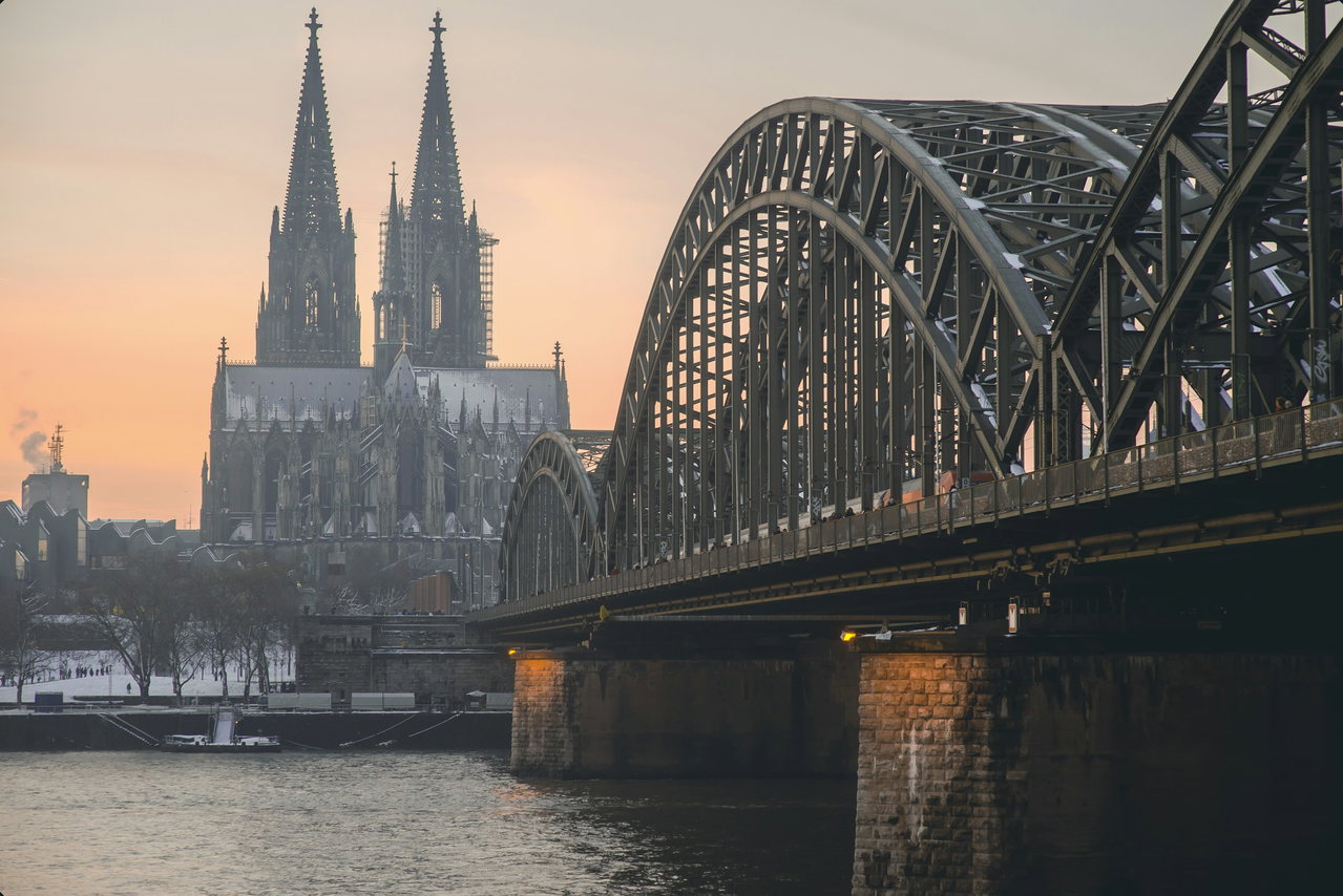 Kölner Dom und Hohenzollernbrücke über dem Rhein bei Sonnenuntergang mit pfirsichfarbenem Abendhimmel