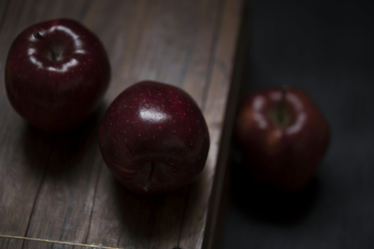 Zwei dunkelrote Äpfel liegen auf einem alten, dunklen Holztisch