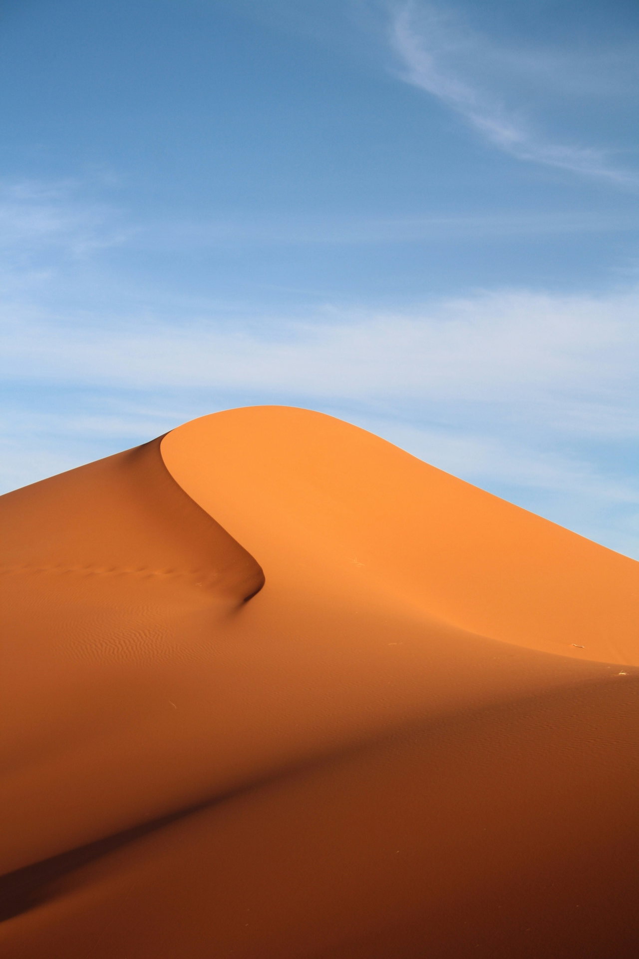 Orangefarbene Sanddüne vor blauem Himmel
