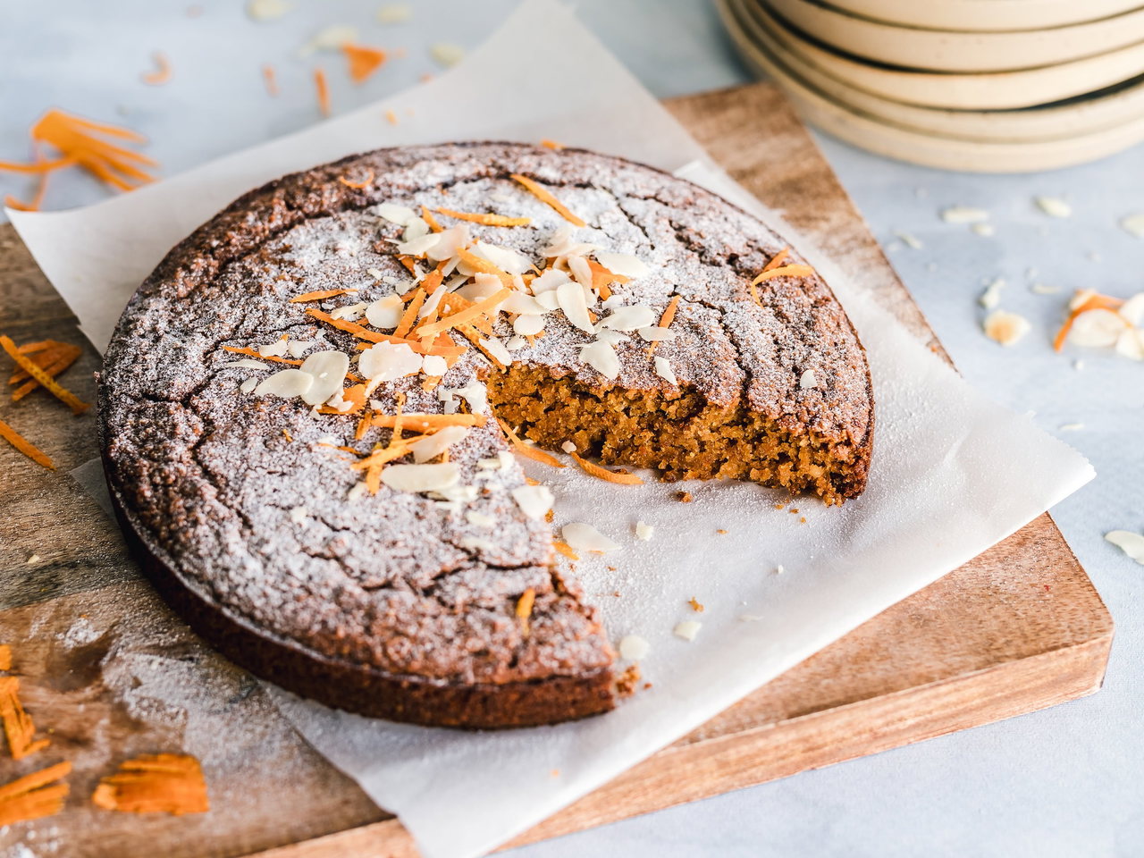 Angeschnittener Karottenkuchen mit Karottenstreifen und Mandelblättchen auf Backpapier
