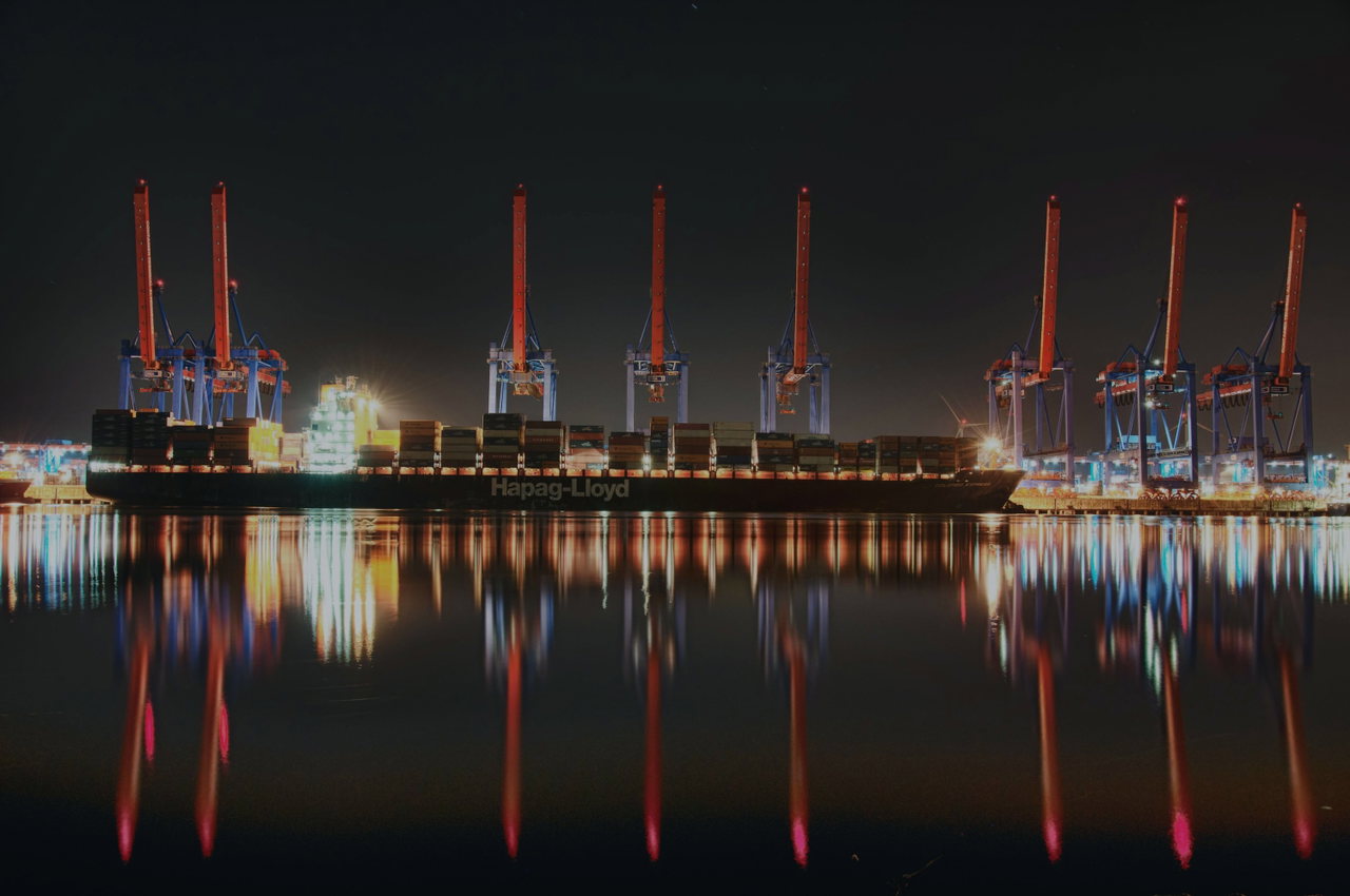 Containerterminal bei Nacht, die Lichter spiegeln sich im Wasser