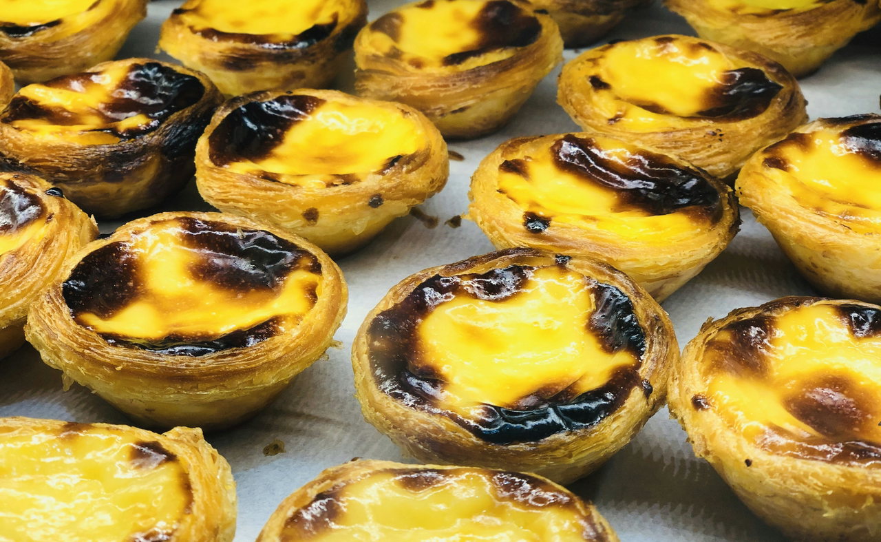 Frisch gebackene Pastéis de Nata mit karamellisierter Oberfläche dicht nebeneinander auf einem Blech