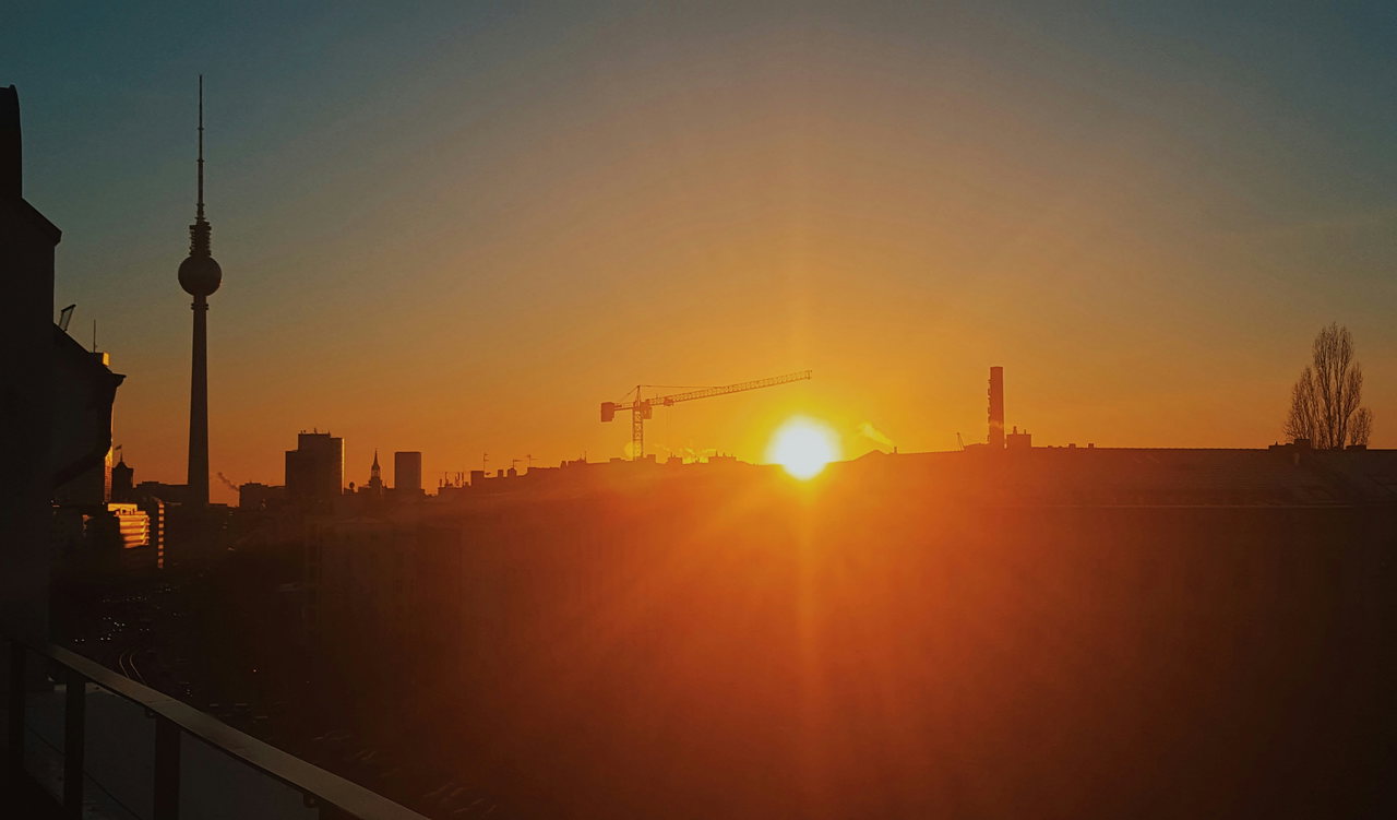 Silhouette der Stadt mit Fernsehturm und Baukran vor der tief stehenden Sonne