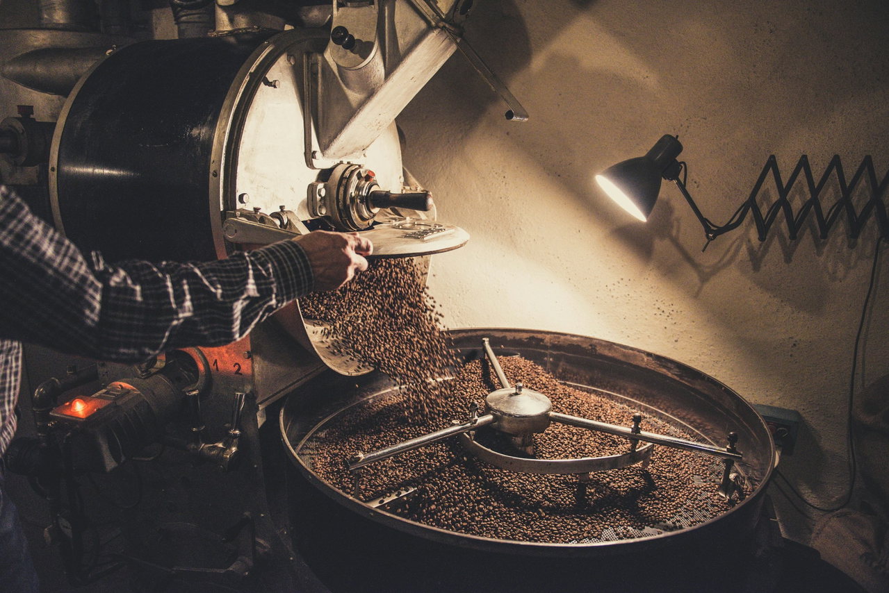Frisch geröstete Kaffeebohnen rieseln aus der Trommel eines alten Röstofens, beleuchtet von einer Wandlampe.