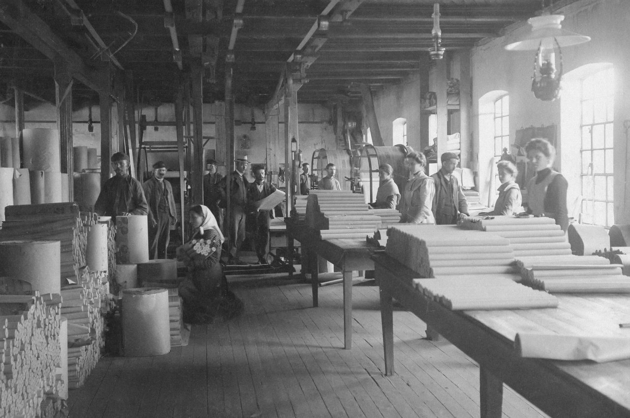 Historisches Schwarz-Weiß-Foto: Arbeiter an langen Werkbänken in einer Holzwerkstatt