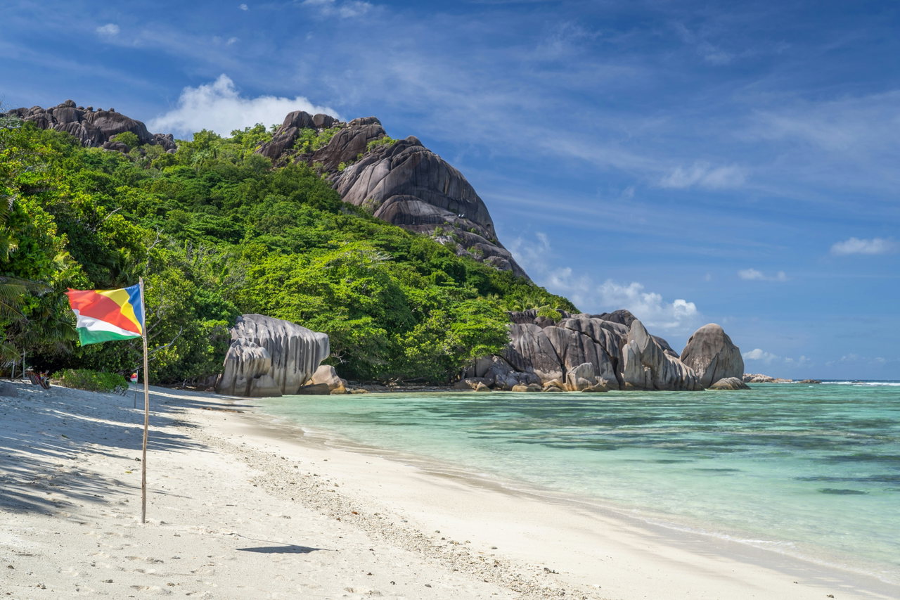 Palmenstrand mit Granitfelsen und der Flagge der Seychellen