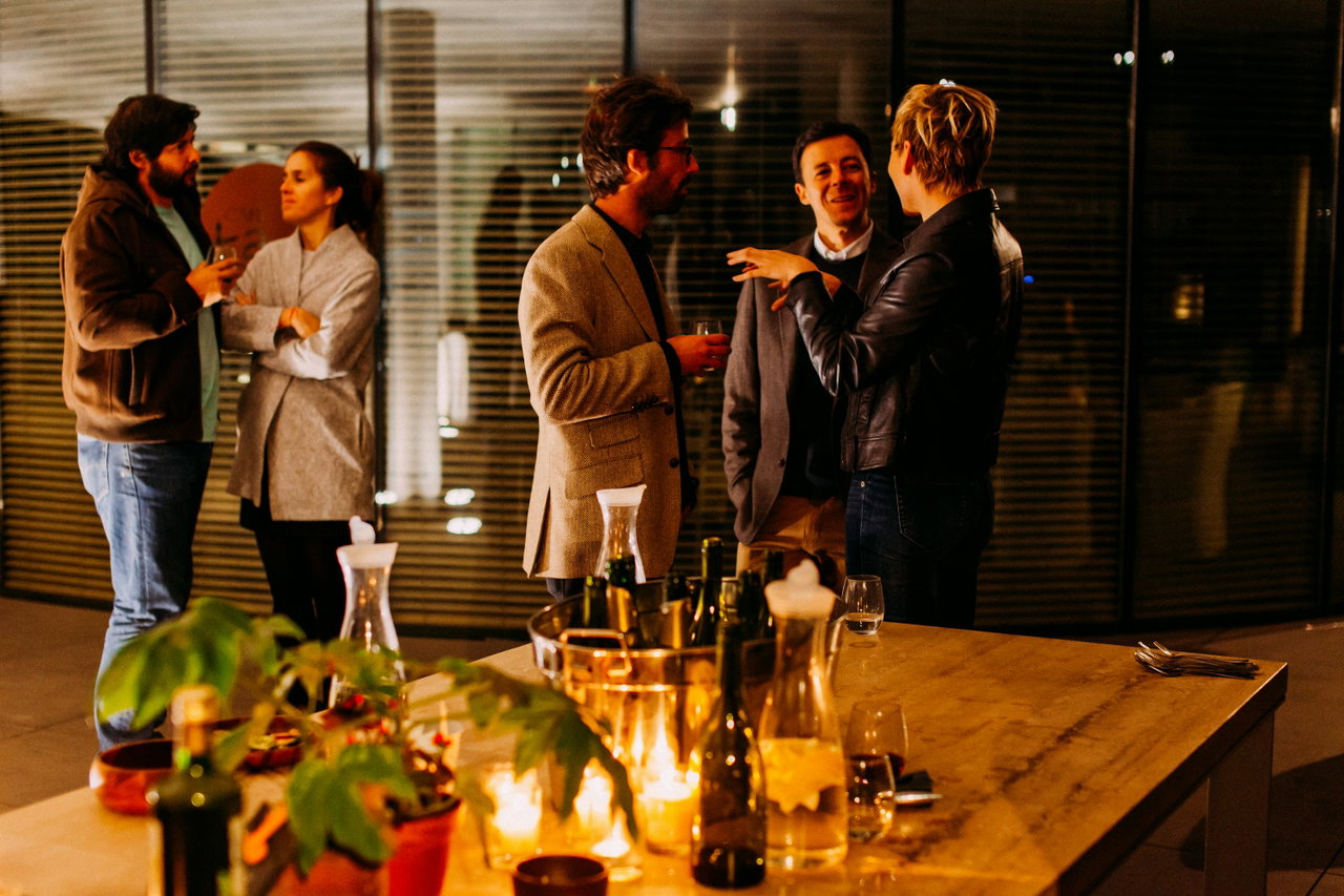 Abendliches Get-together mit Gesprächen an einem Holztisch, Kerzenlicht, Gläsern und warmem Licht