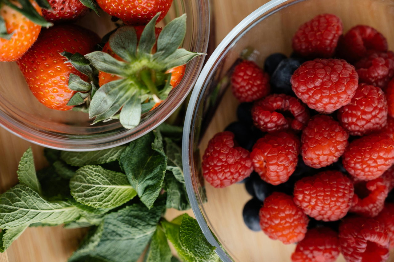 Schalen mit frischen Erdbeeren und Himbeeren, dazwischen Minze