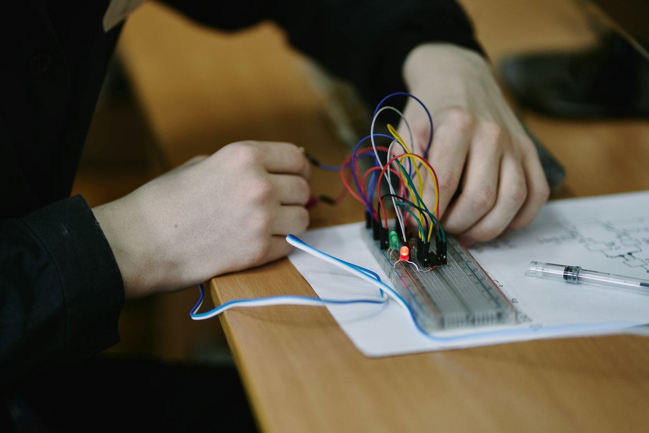 Hände verdrahten auf einem Steckbrett eine Schaltung nach einem Schaltplan, praktische Übung in der Ausbildung