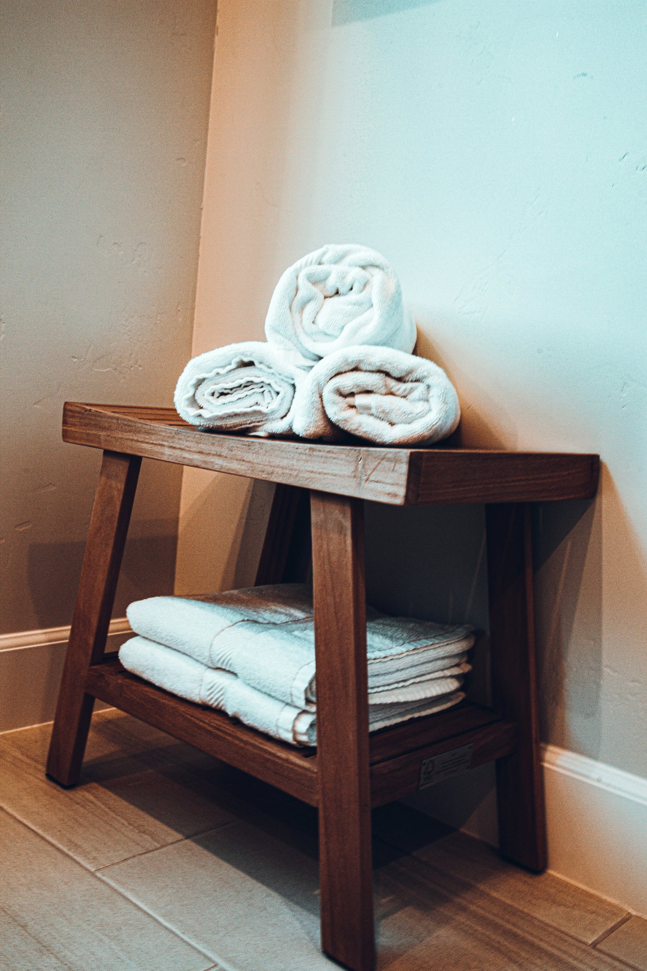 Zusammengerollte Handtücher auf einem dunklen Holzhocker mit weiteren Handtüchern im Regal in einem Spa-Raum