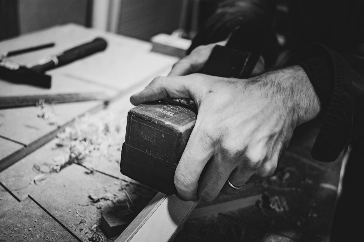 Schwarz-Weiß-Foto: Eine Hand führt einen Hobel über ein Brett