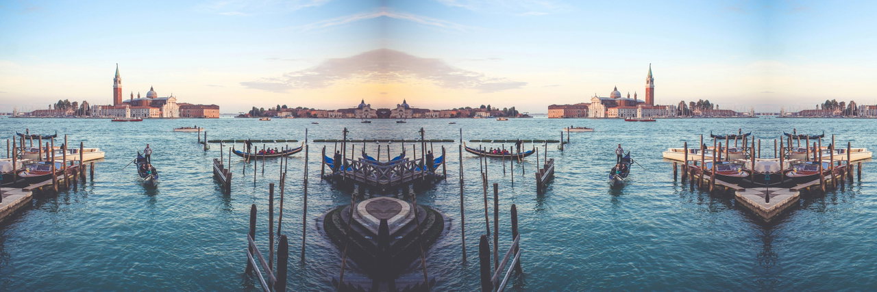 Blick über die Lagune von Venedig auf San Giorgio Maggiore, davor eine Gondel und Anlegepfähle im Abendlicht
