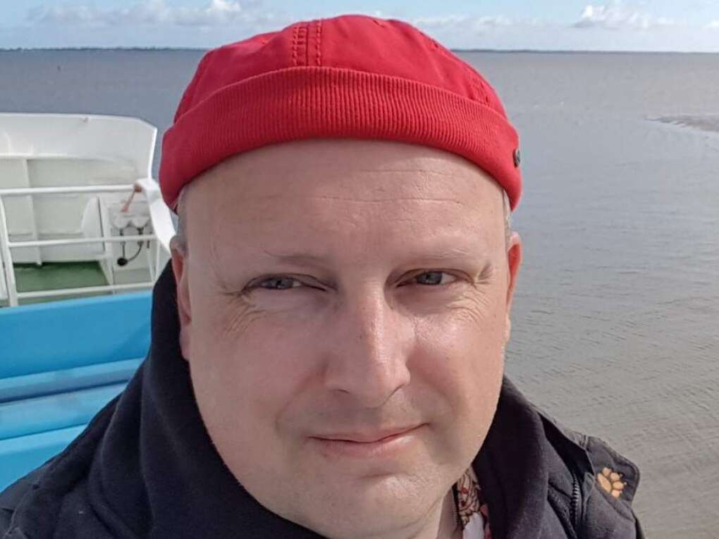 Mann mittleren Alters mit roter Mütze und blauer Jacke auf einer Fähre