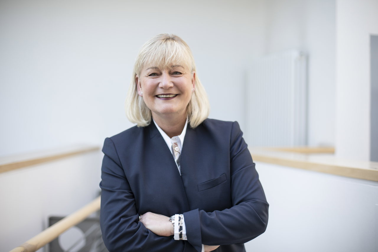 Kerstin-Mosig-in-einem-Blazer-steht-vor-einer-weißen-Wand