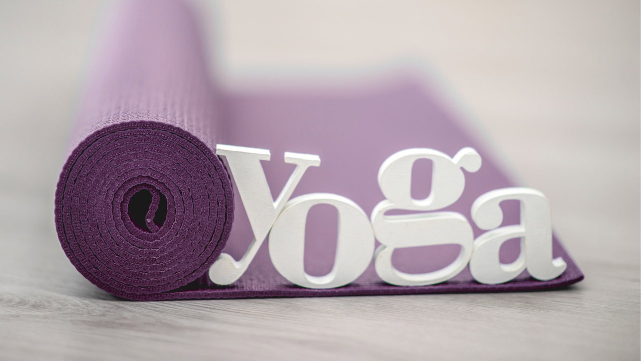 Diese Bild dient als Hintergrund. Es zeigt eine abgerollte Yogamatte mit einem Yoga-Schriftzug aus Holz.