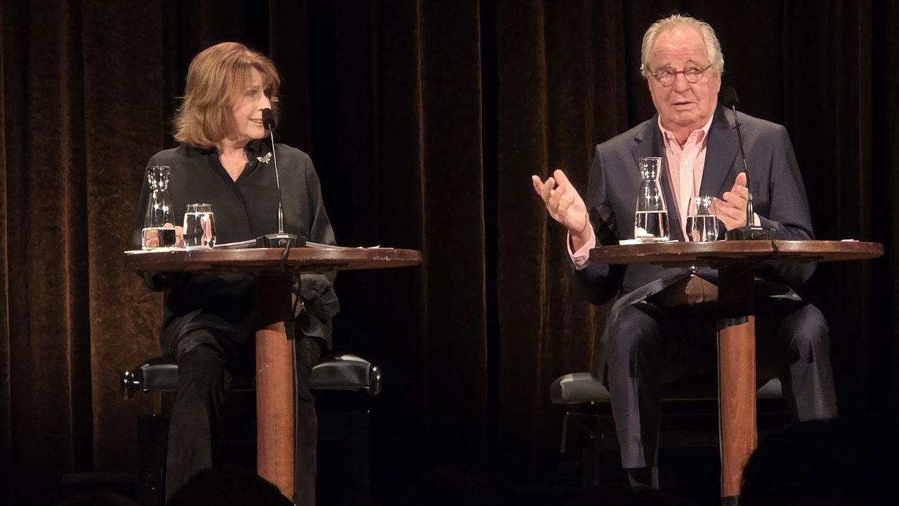 Senta Berger (eine bekannte Schauspielerin) und Friedrich von Thun ( sitzen an kleinen runden Tischen auf einer Bühne und lesen.
