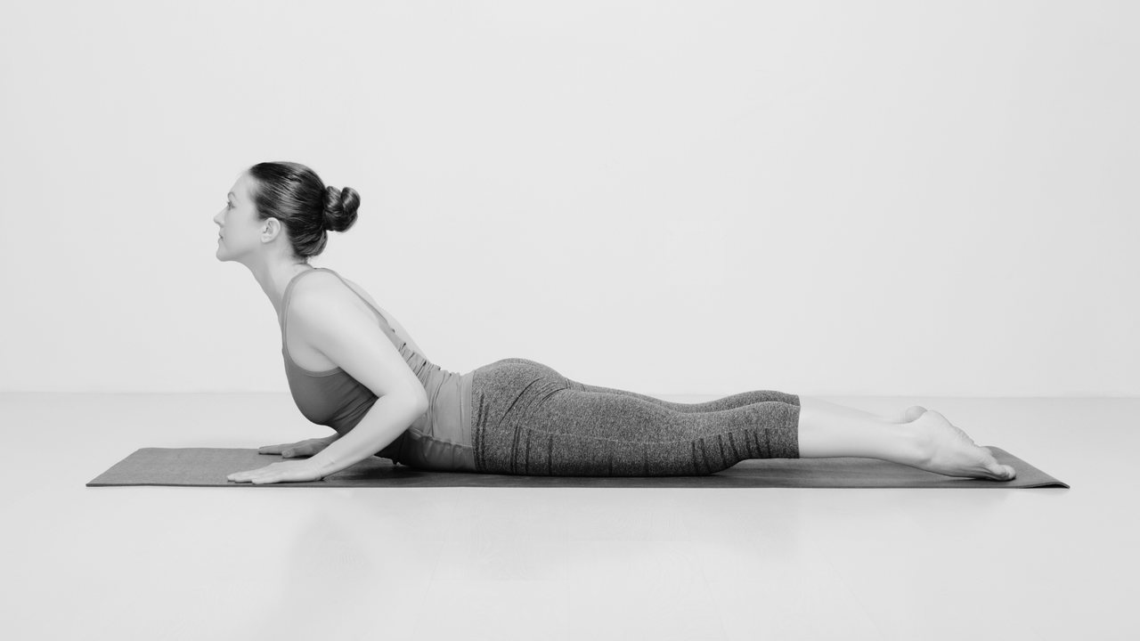 Diese Bild zeigt eine Frau auf einer Yoga-Matte in der Position "Kleine Kobra".