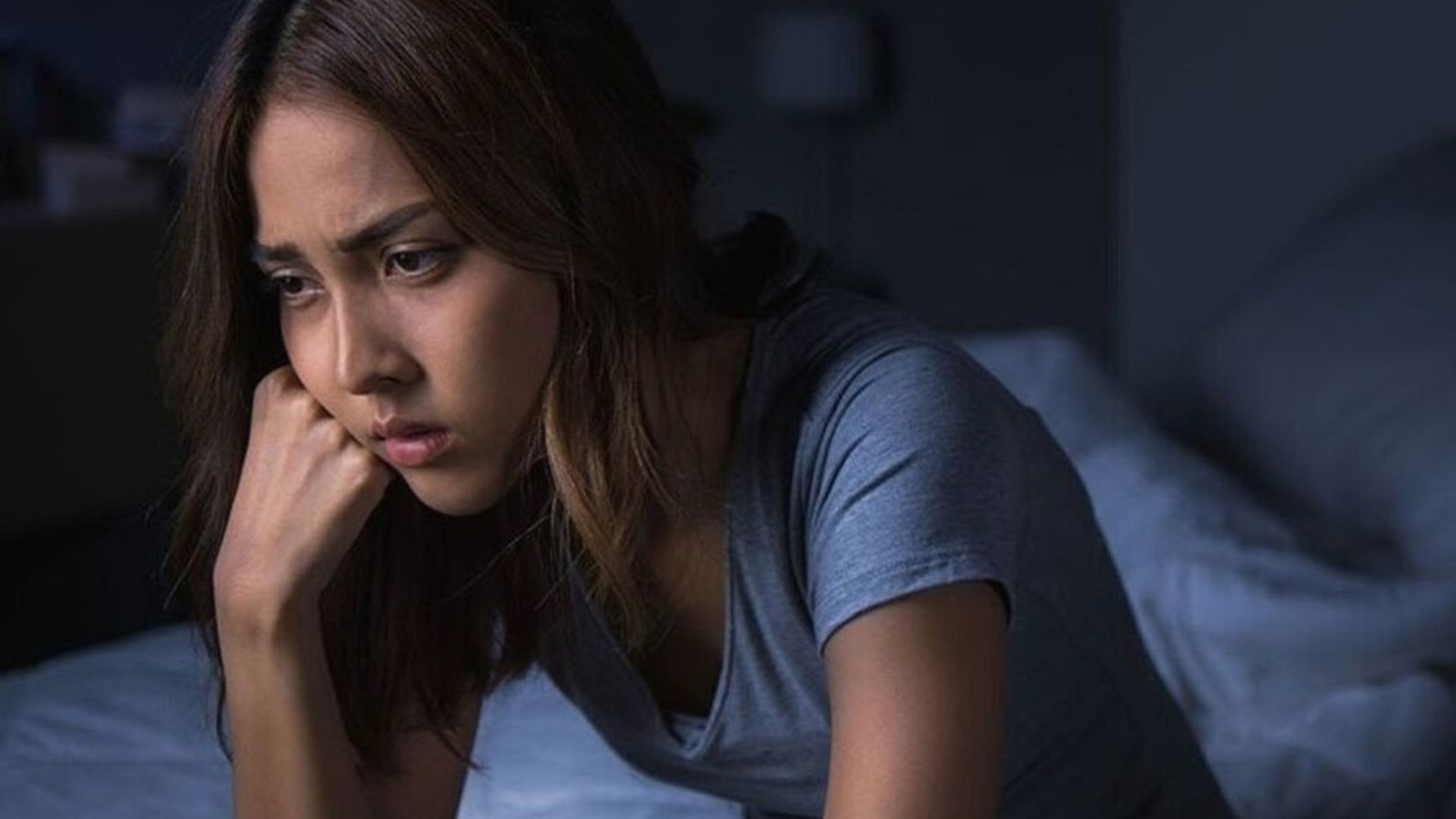 Eine Frau sitzt nachdenklich auf der Bettkante.